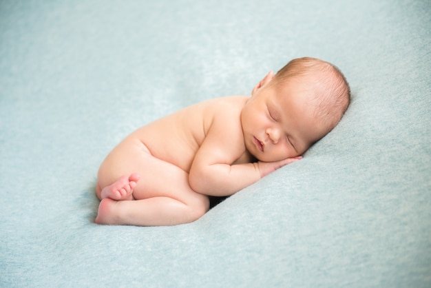 A newborn baby is peacefully sleeping naked. Hands behind his head