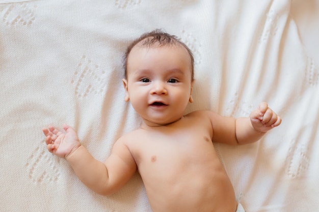 Новорожденный ребенок лежит на белой простыне без одежды и улыбается