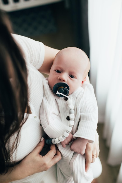 Newborn baby in light clothes in the arms of the mother