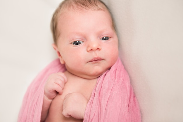 Newborn baby looks down in a pink blanket