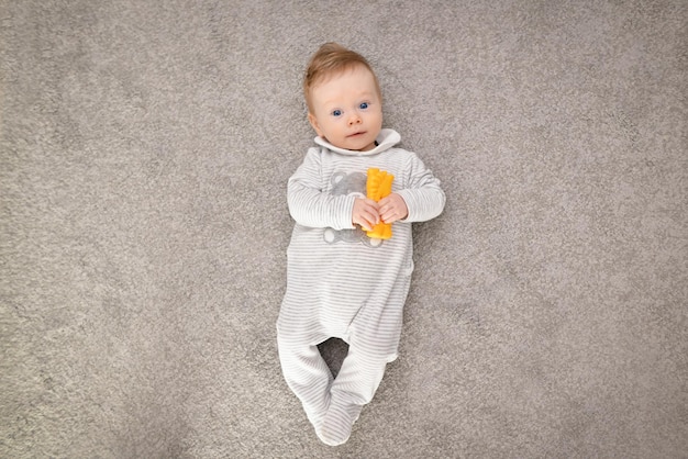 Photo newborn baby lying on the carpet with toy pretty young boy playing