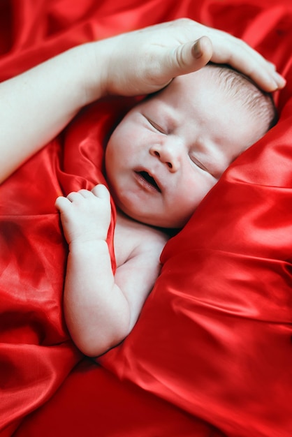 Newborn baby lying on a red silk fabric