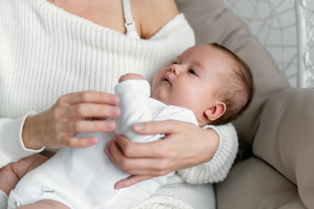 Newborn baby in mom's arms. They sit on a wicker chair on a soft cushion. Protection of children.