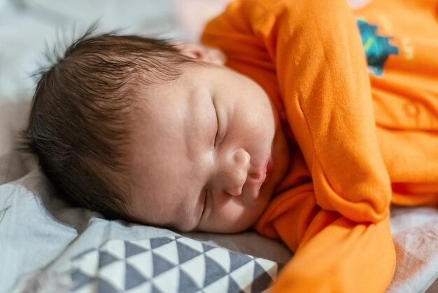 Newborn baby in orange closes sleeps in his bed