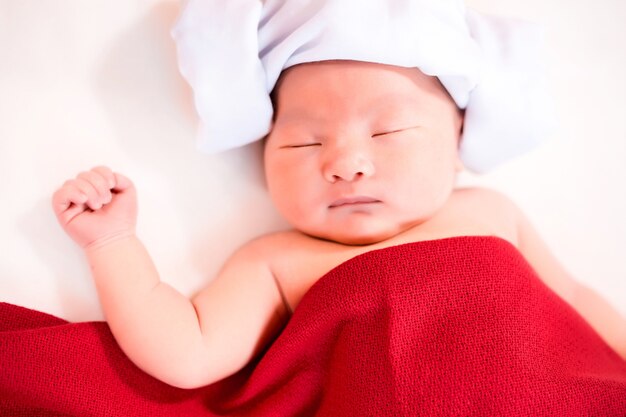 Newborn baby in red daiper sleeping on bed