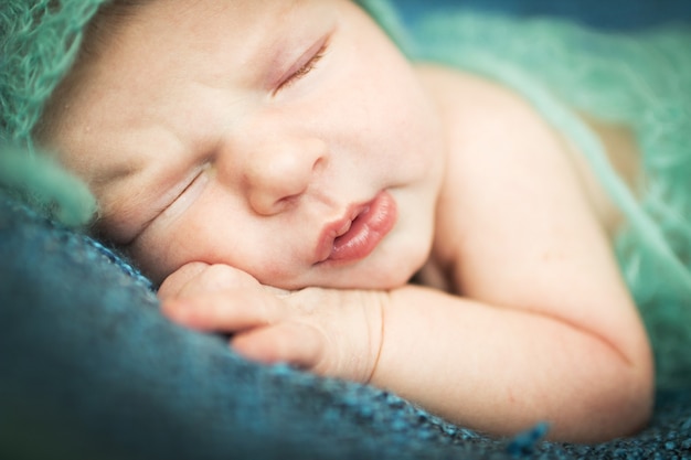 青い帽子の青い敷物の上で甘く眠っている生まれたばかりの赤ちゃん