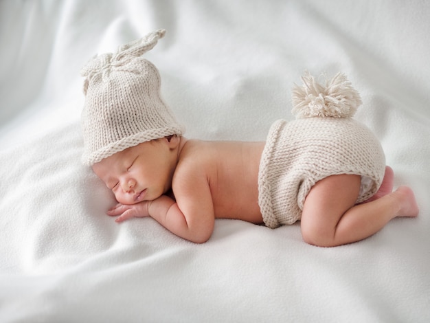 Foto neonato che dorme e indossa abiti di coniglio all'uncinetto, sfondo bianco. concetto di neonati e nuova vita.