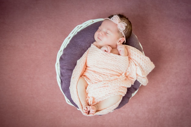 Newborn baby sleeps in a basket in a pink blanket