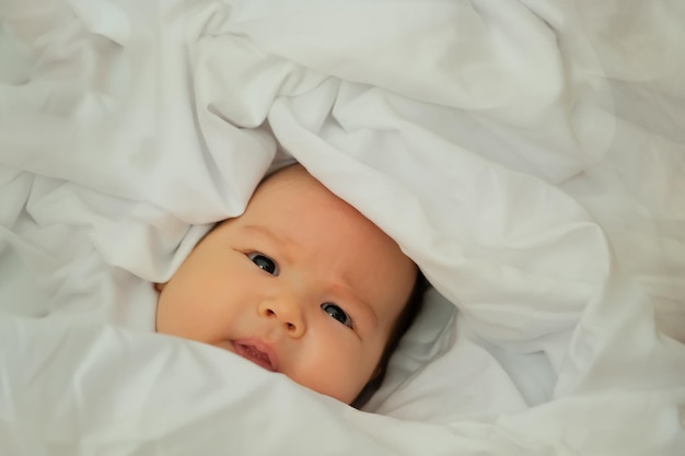 Newborn baby smiles and laughs shows emotions baby lies on a white cloth