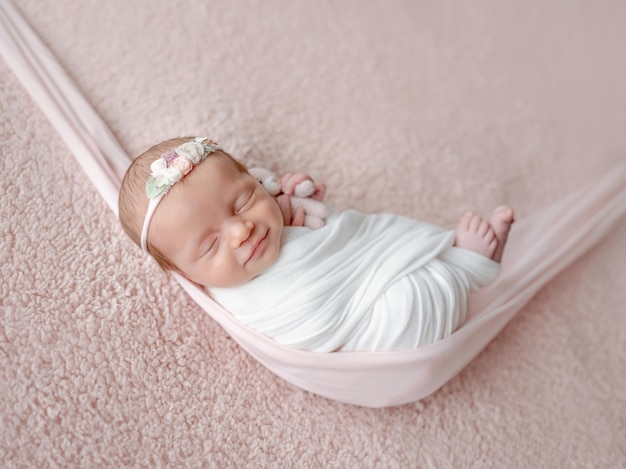 Newborn baby swaddled in a blanket sleeps in a hammock during a photo session with a smile