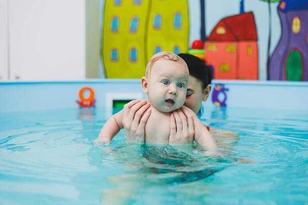 A newborn baby swims in the pool Teaching children to swim A baby learns to swim in a pool with a trainer Baby learning to swim Child development