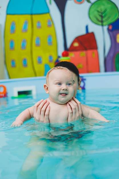 Новорожденный ребенок плавает в бассейне. Обучение детей плаванию. Ребенок учится плавать в басейне с тренером. Ребенок изучает плавание. Развитие ребенка