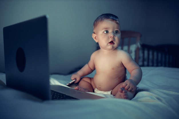 Photo a newborn baby uses a computer while sitting on a sofa at night. the child is dressed in a diaper on his naked body.