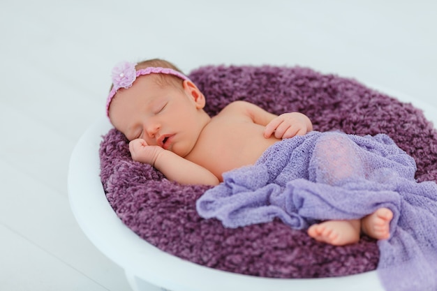 Newborn baby in violet knitted suit sleep in wooden basket