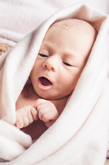 Newborn baby wrapped in beige blanket.