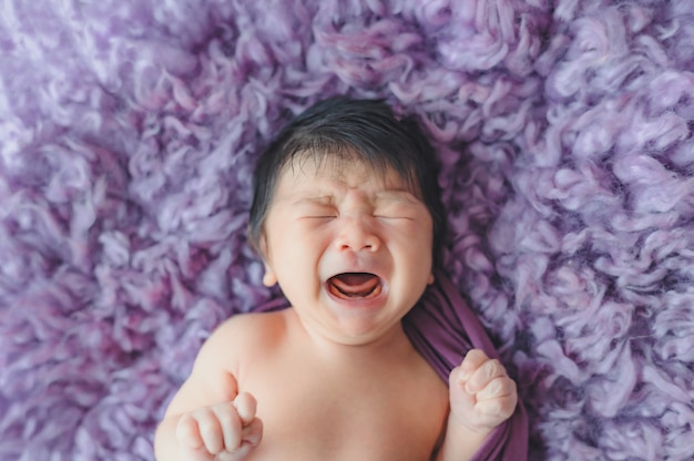 Newborn boy crying while sleeping on purple fur bed