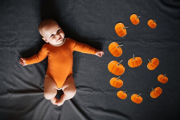 Newborn boy lies with pumpkins denoting six months