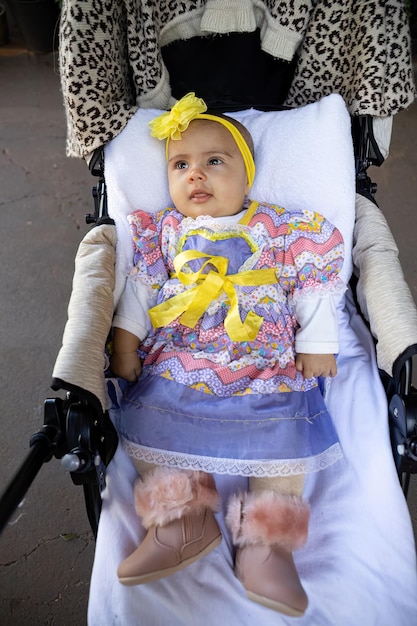 写真 新生児の女の子がベビーキャリッジで頭の上にパーティー服と黄色い弓をかぶっています