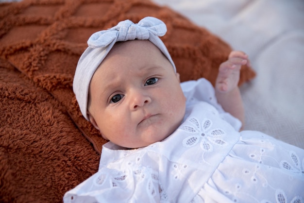 A newborn child lies on a blanket on the shore flowers lie nearby