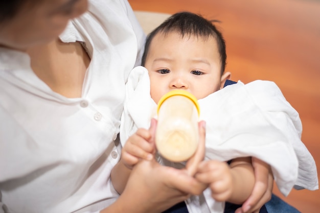 Newborn cute baby is drinking milk from bottle by mom