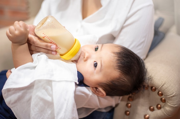 Newborn cute baby is drinking milk from bottle by mom