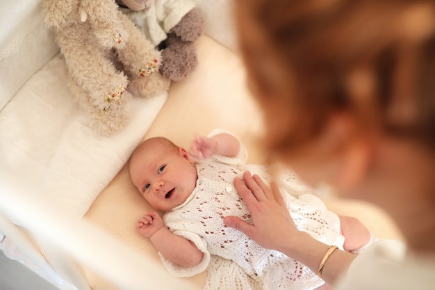 Newborn cute baby lies in the crib and looking at mother