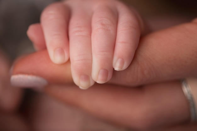 A newborn holds on to mom's, dad's finger. Hands of parents and baby close up. A child trusts and holds her tight. . High quality photo