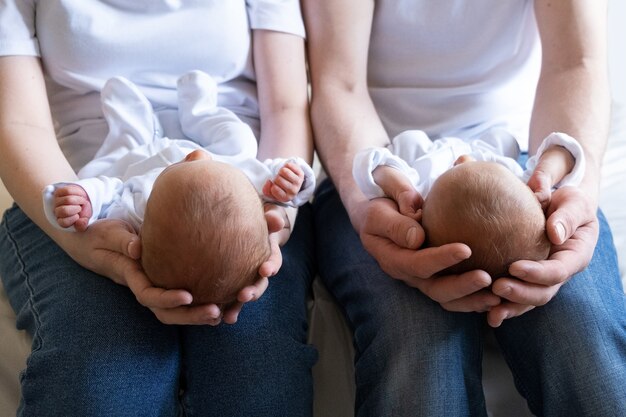 両親の手でベッドの上に生まれた一卵性双生児子供たちのライフスタイルの感情コピースペースを持つ幼児の赤ちゃん