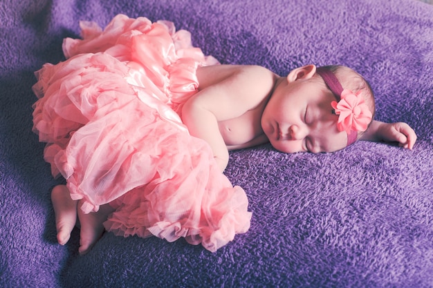 Newborn pretty baby girl in pink tutu dress sleeps on the purple textile