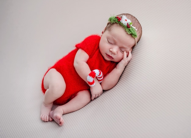 Newborn in red suit holding knitted christmas cane candy