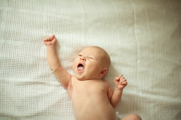 новорожденный улыбающийся ребенок в белых пеленках