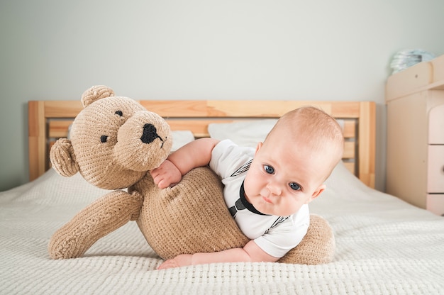 Newborn toddler with a toy bear on the bed close-up and copy space. Funny baby and soft toy bear