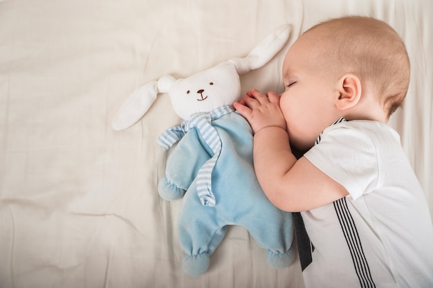 Newborn toddler with a toy on the bed close-up and copy space. The child sleeps on a large bed