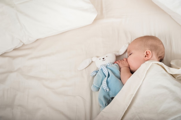 Newborn toddler with a toy on the bed close-up and copy space. The child sleeps on a large bed