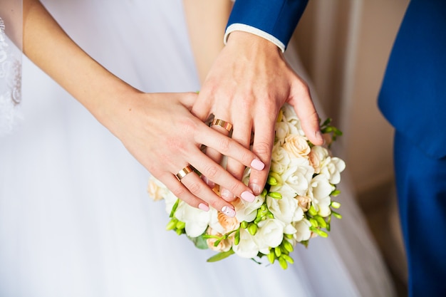 A newly weding couple place their hands on a wedding bouquet showing their wedding rings.