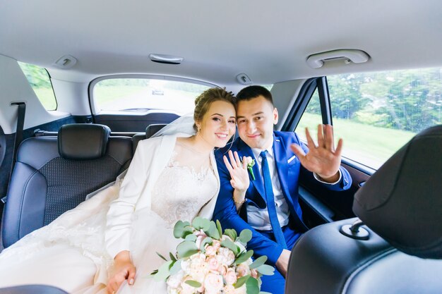 Newlyweds are sitting in the car looking at the camera