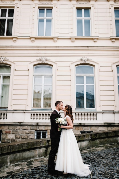 新婚夫婦は立って抱き合って、古代の復元された建築物、古い建物、外の古い家、屋外のヴィンテージの宮殿の近くでキスをしています。