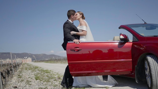 Newlyweds by the convertible car feelings of tenderness action man in suit helps the bride to leave