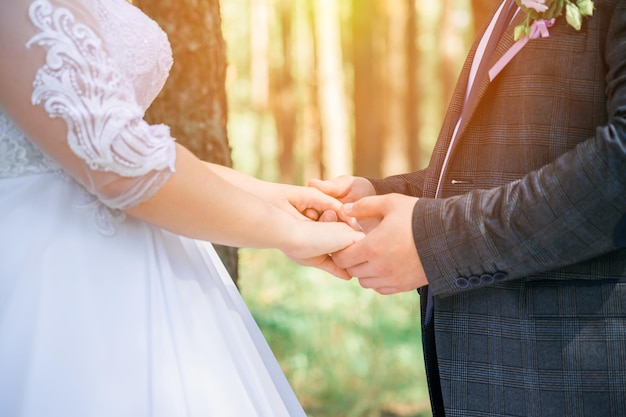 The newlyweds in the forest hold each other's hands in the sunlight