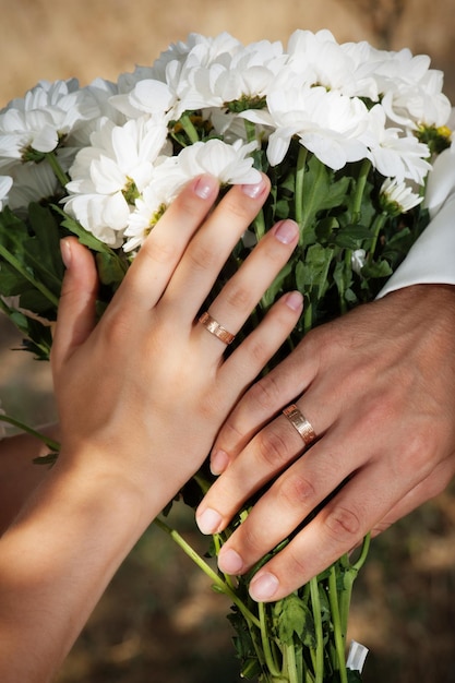 Newlyweds hands with wedding rings on the bouquet with simple white flowers