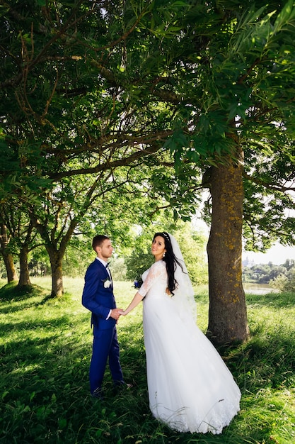 Newlyweds hold hands in park and bride posing