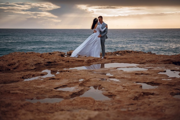 The newlyweds pose in wedding clothes on the rocks by the sea Beautiful young couple tenderly embracing Newlyweds wedding on the island