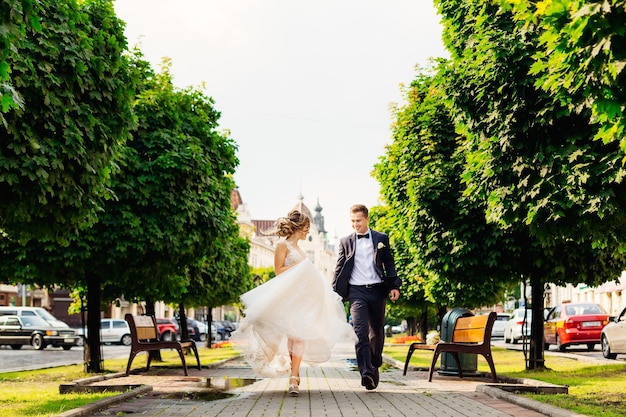 Newlyweds running along the sidewalk and looking at each other in the city