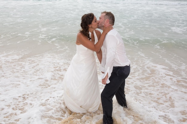 Sposi novelli che condividono un momento romantico in spiaggia che si baciano