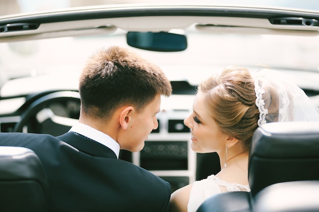 Newlyweds smile at each other while sitting in a convertible close up
