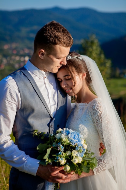 Newlyweds smile and hug each other among the meadow on top of the mountain. Wedding walk in the woods in the mountains, the gentle emotions of the couple