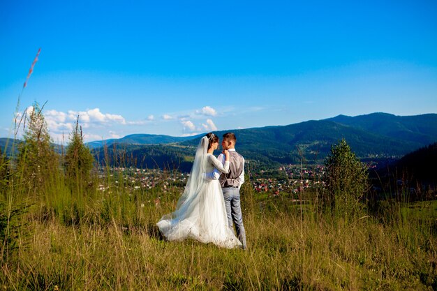 新婚夫婦は山の頂上にある牧草地の中で笑顔で抱き合っています