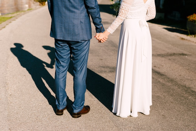 Gli sposi stanno sulla strada tenendosi per mano il sole splende brillantemente dietro le loro sagome di sposa e