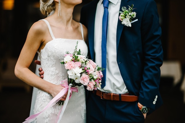 Newlyweds standing and holding bouquet of pink and purple flowers and greens with ribbon at the wedding ceremony