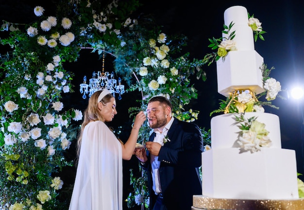 Photo newlyweds tasting wedding cake on evening ceremony